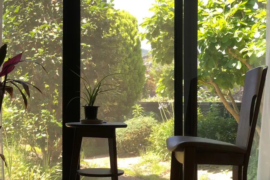 Bodentiefe Fenster mit Blick in einen grünen Garten, davor ein Stuhl und Zimmerpflanzen