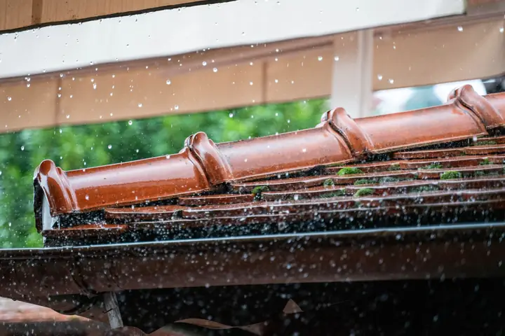 Rote Dachziegel mit Regenrinne am Hausdach, Wasser tropft herab